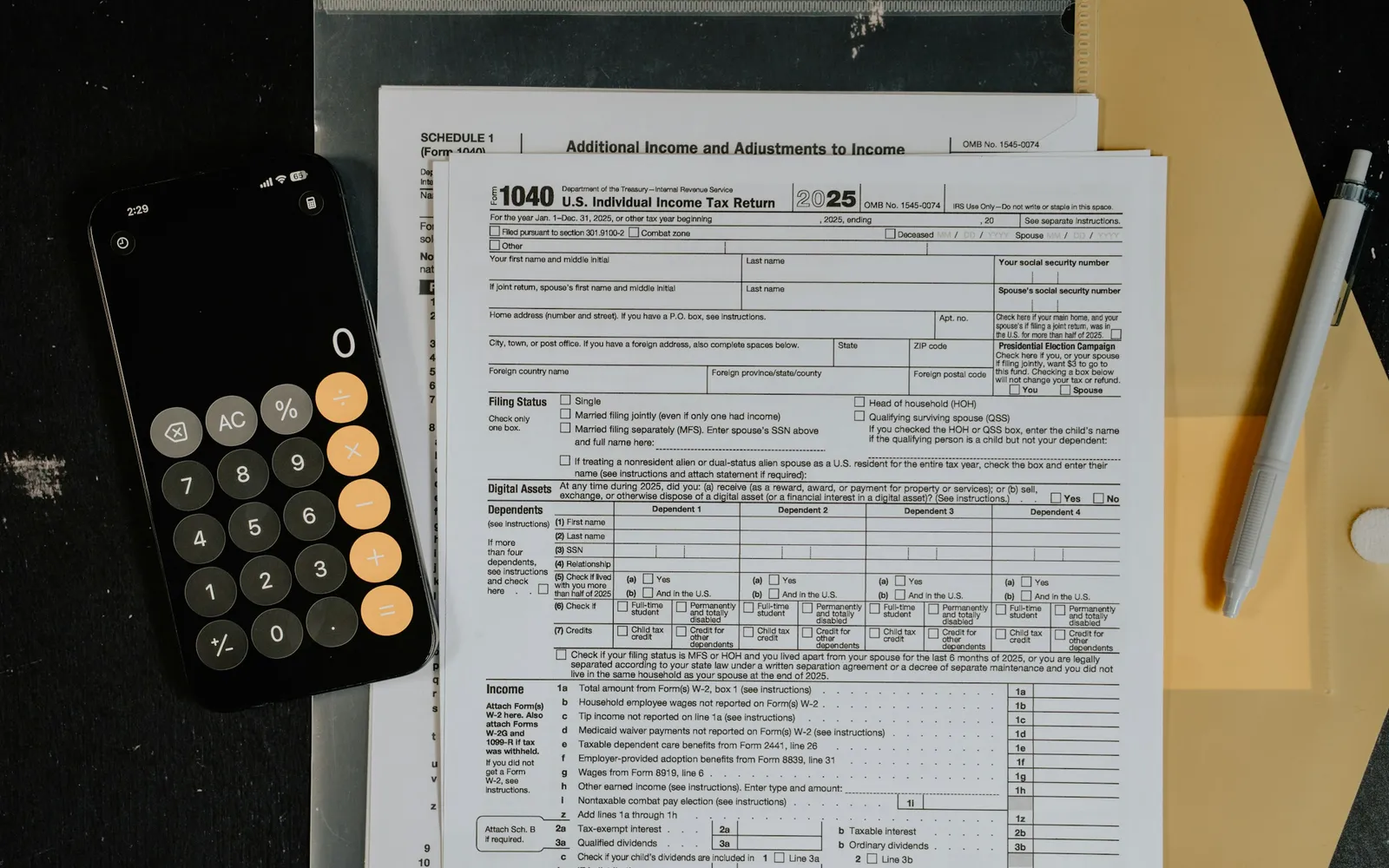 Tax forms, a phone calculator and a pencil on a dark desk