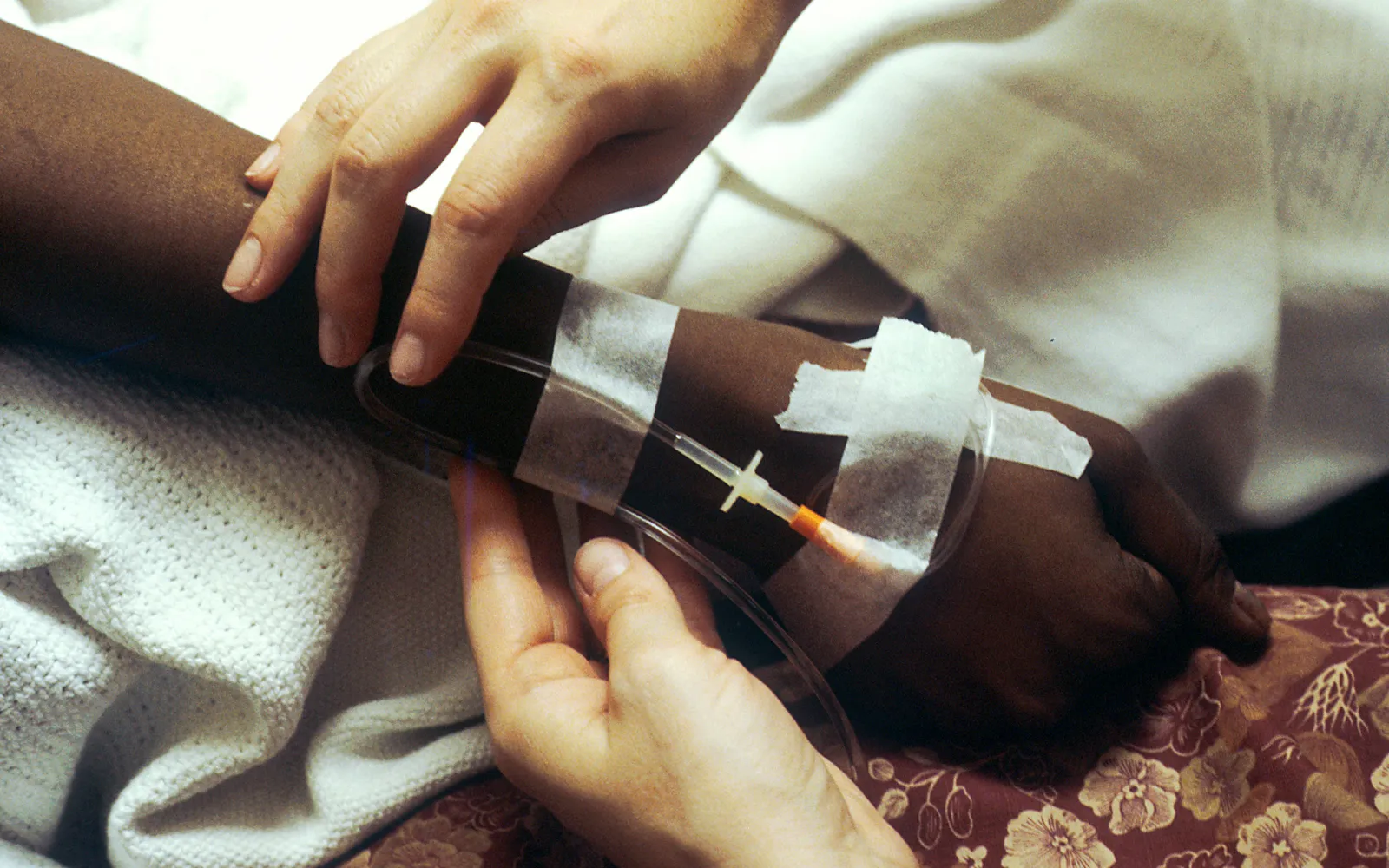 Two hands adjust an IV line for chemotherapy in a patient's arm