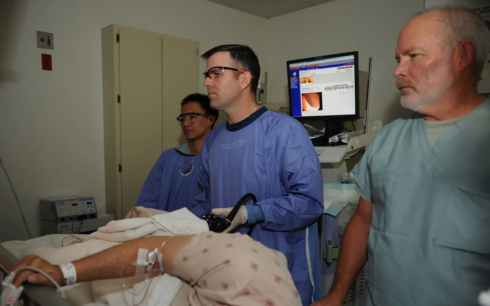 A Navy doctor and two staff members watch a monitor showing the inside of a colon during a colonoscopy