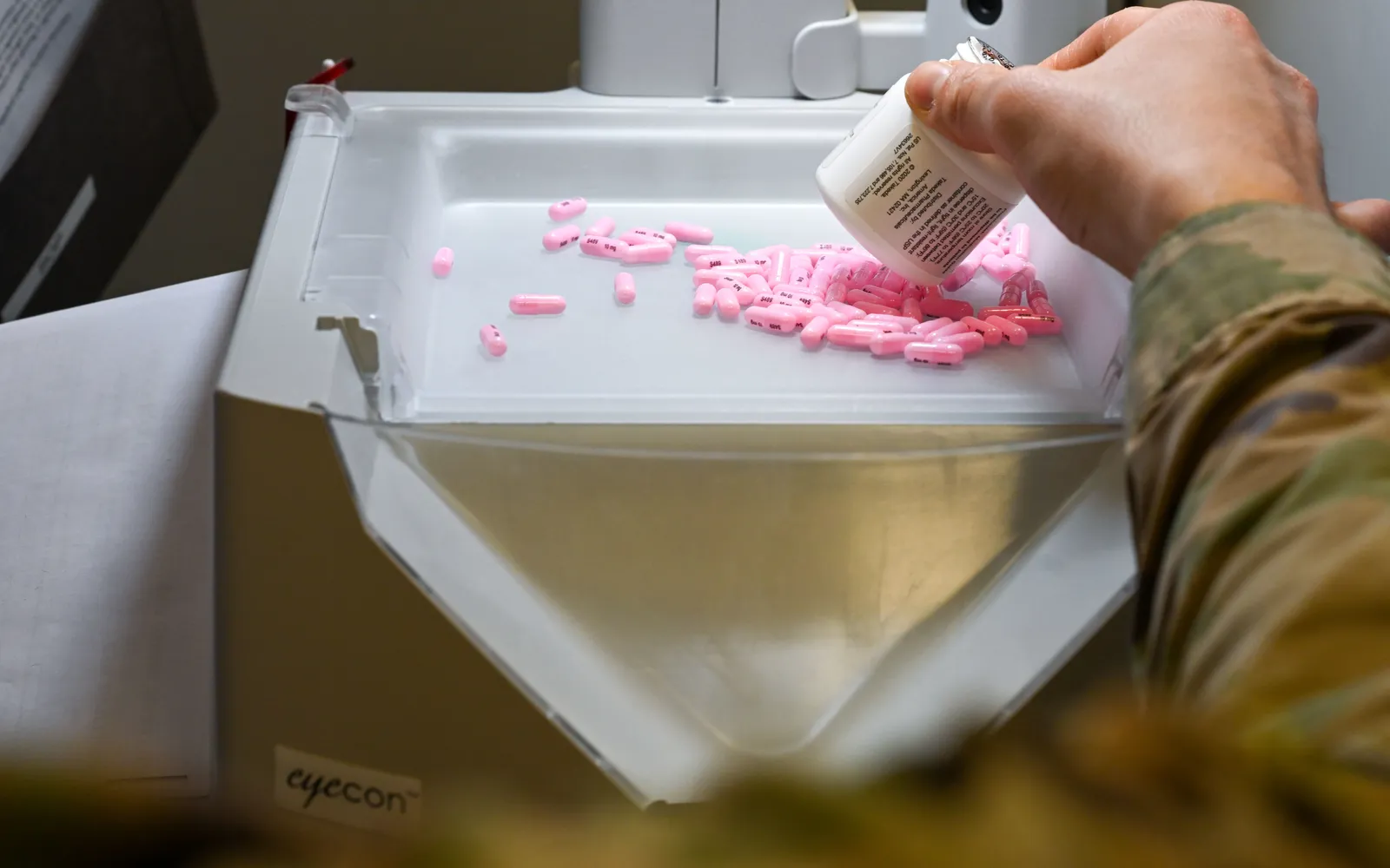 A pharmacist pours capsules into an automated pill counter at a pharmacy counter