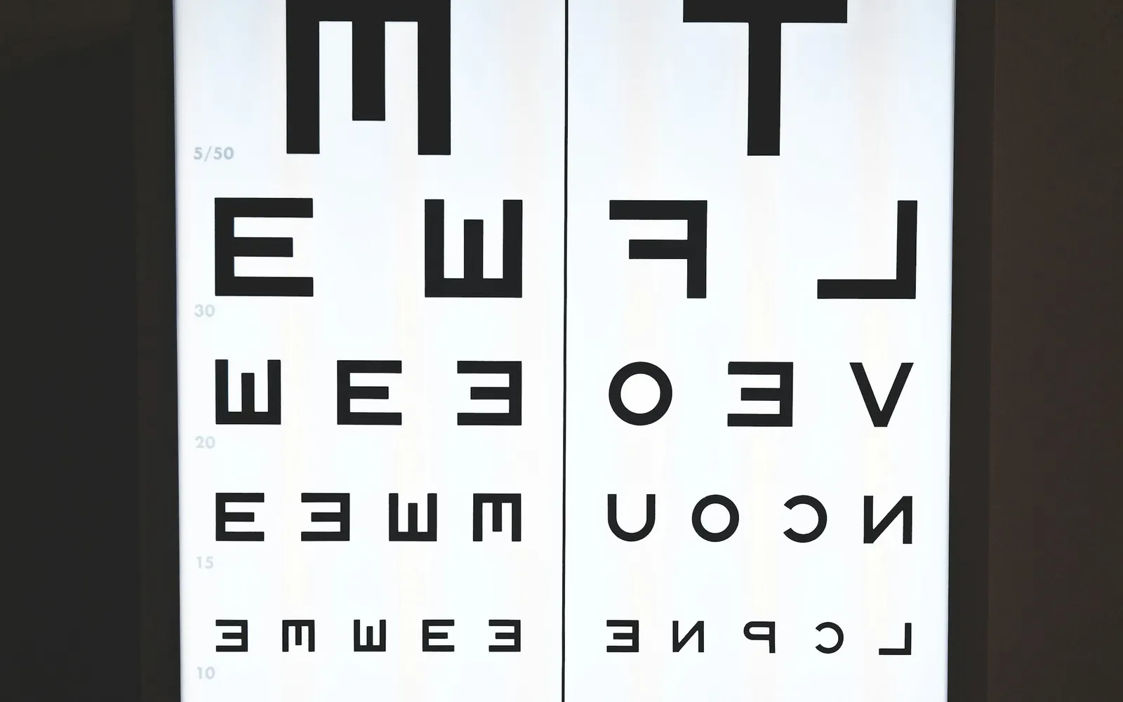 A backlit eye chart with rows of letters on a dark wall