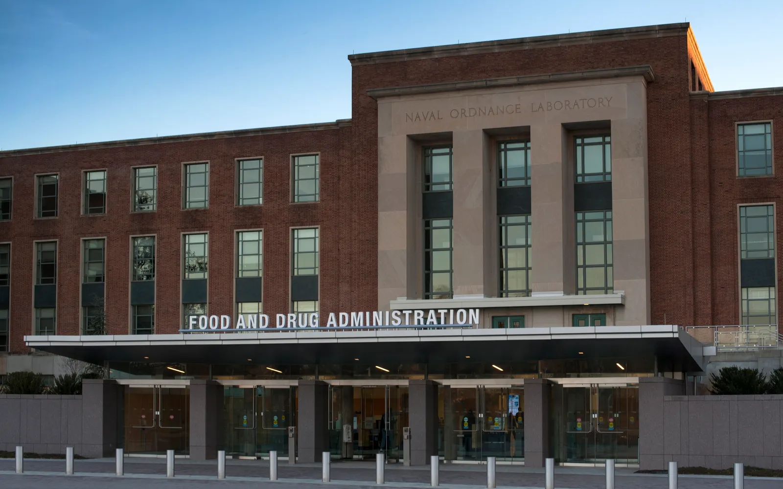 The lit main entrance of FDA Building 1 at dusk, with FOOD AND DRUG ADMINISTRATION in steel letters over the canopy