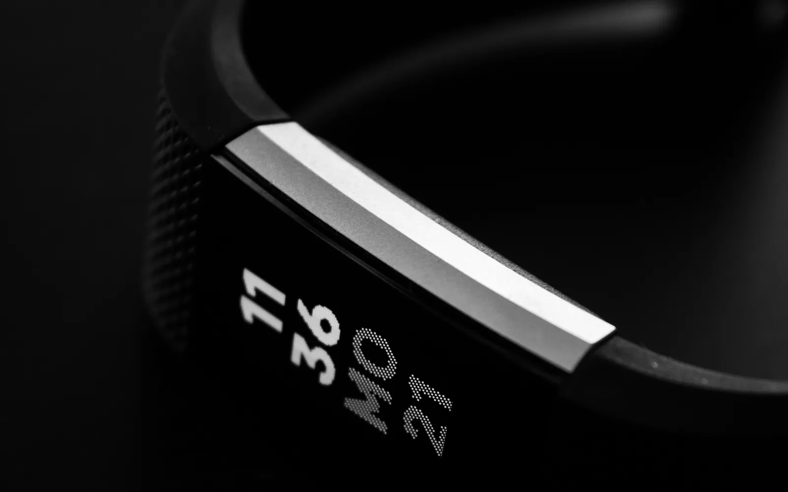 A black fitness tracker band in low light, its screen showing 11 36 and MO 21