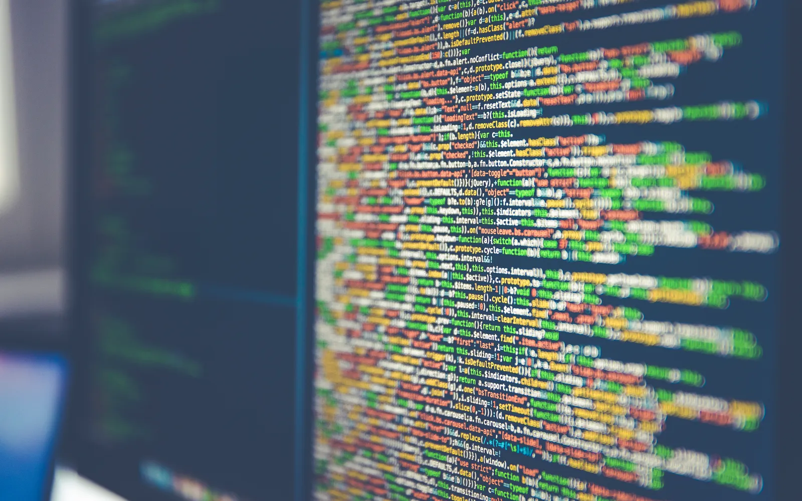 Colorful lines of software code glowing on a dark computer monitor, shot at an angle with shallow focus