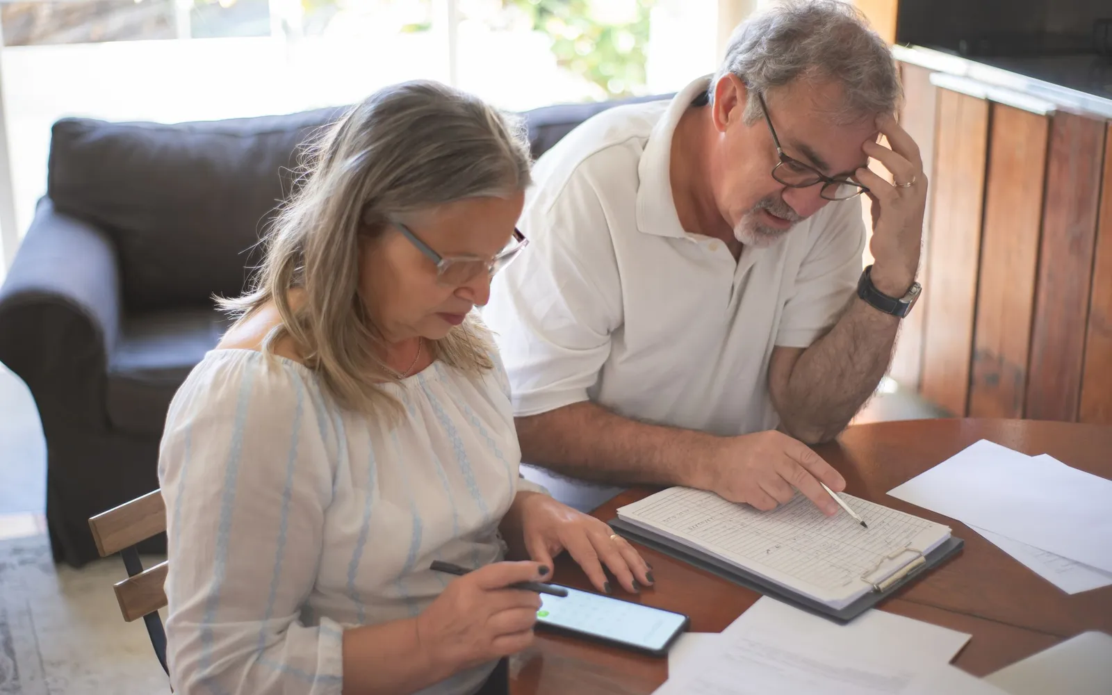 An older couple at a table going over papers, one holding a pen and a phone
