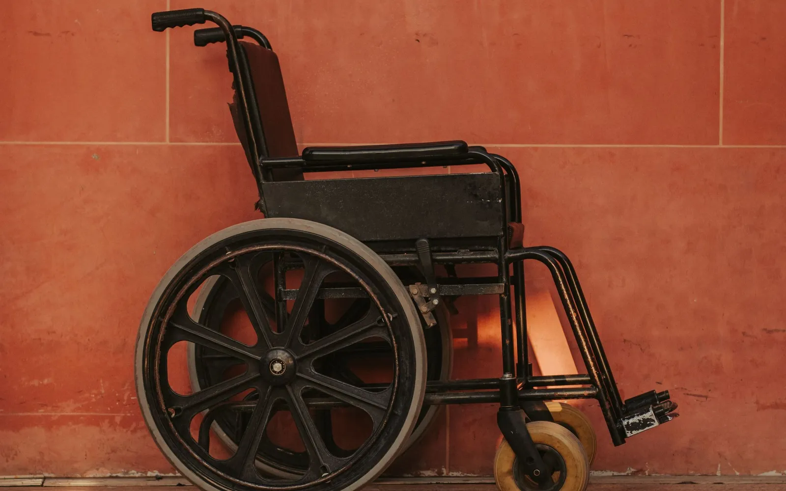 An empty black wheelchair against a bright red wall