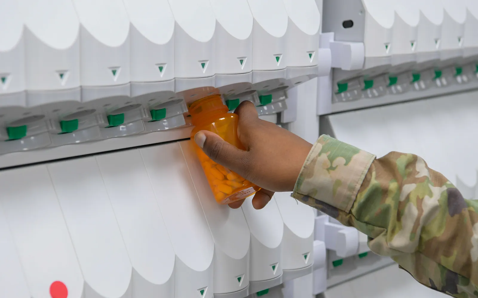 A hand places an orange prescription bottle into an automated pharmacy dispensing machine