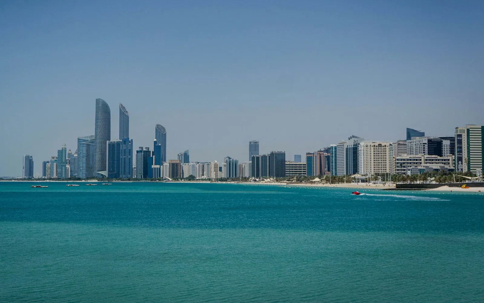 The Abu Dhabi skyline and Corniche beach across turquoise water under a clear sky