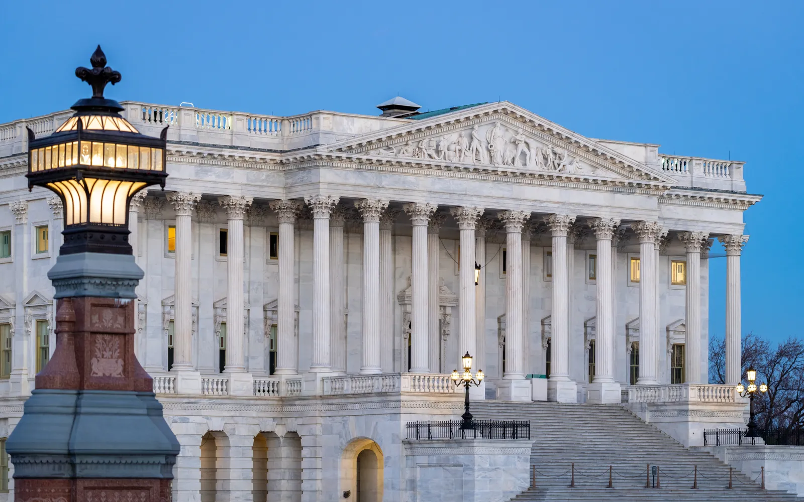 The Senate wing of the U.S. Capitol at dawn, a lit lamp post in the foreground